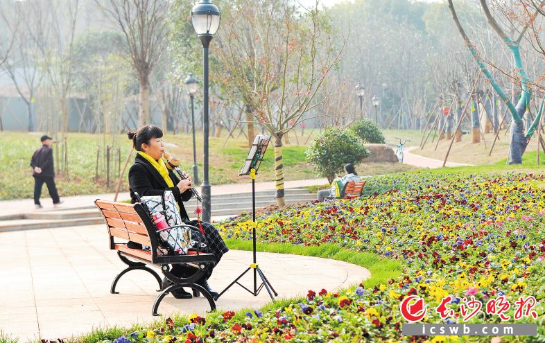 在雨花区井巷社区公园里，一位居民在优美的环境中吹着葫芦丝，陶醉其中。 邹麟 摄