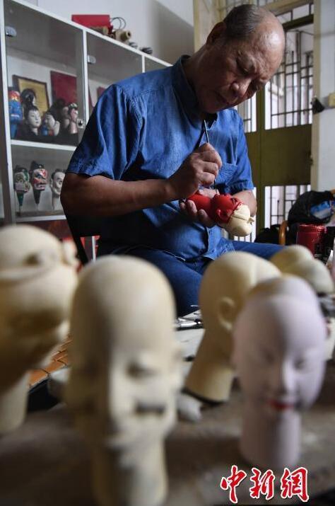 图为杨亚州在其工作室为雕刻的木偶头上色。