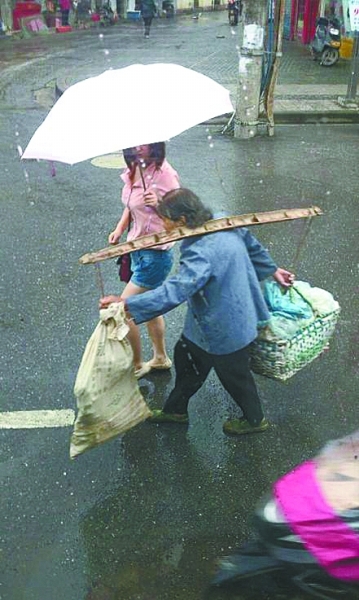 路遇太婆雨天挑担赶路 拿起雨伞举过婆婆头顶