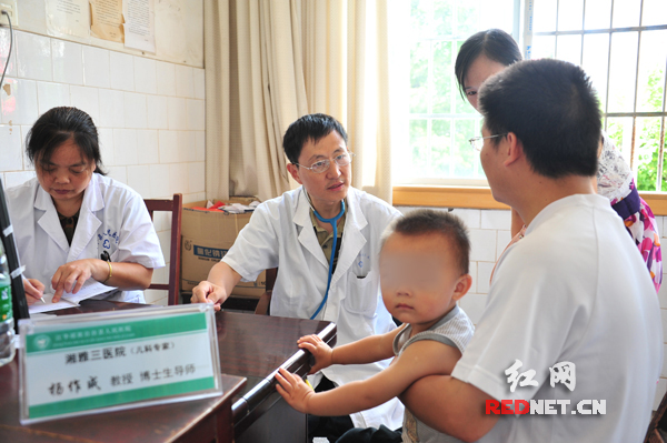 　（湘雅三医院儿科专家杨作成教授(左二)给患儿义诊。）