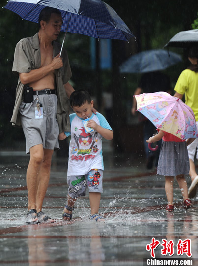 7月1日，重庆市气象台发布“暴雨橙色预警”，气温随之下降，雨水给市民带来一丝凉意。图为一小孩正在踩水。陈超　摄