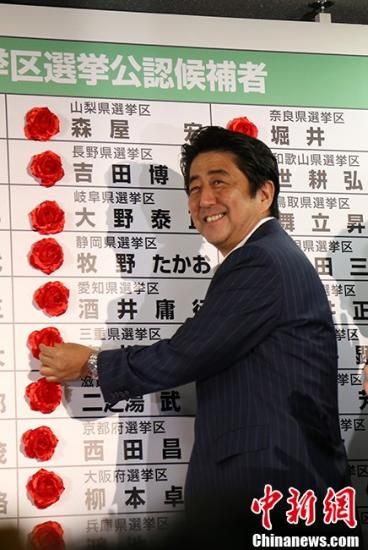 图为日本首相安倍晋三21日晚在自民党总部的开票中心为当选议员贴花。中新社发 高越 摄