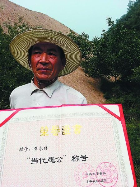 　黄永林手捧“当代愚公”荣誉证书站在矿渣山前。