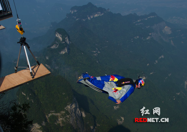 一位翼装飞行选手跳出山顶跳台，开始空中滑翔。