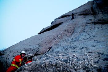 被困者悬在半空中,一组救援人员从山顶扔下了绳子,另一组救援人员在山脚接应。