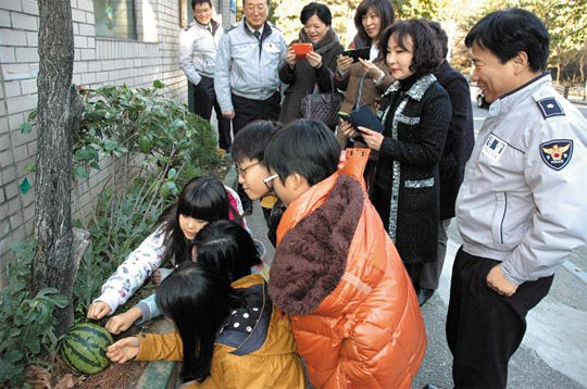 20日，在首尔水西警署开浦派出所举行的切西瓜活动中，首尔浦二小学学生正在敲打在开浦派出所花坛里长出的西瓜。当天参加活动的居民和警察吃掉了这个西瓜。