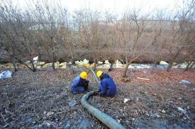 路边排水沟水面上铺了大量吸油纸，工人正在安装抽水管进行油水分离作业。