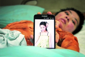 躺在病床上的英子翻出手机里的艺术照。 　　信息时报记者 康健 摄