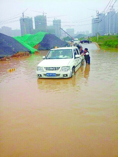 5月5日8点多，在长沙梅溪湖路地铁口边，刘先生的小车在积水中熄火，附近市民帮他将车推出。(读者供图)
