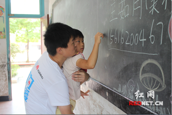 支教队员抱起一名学生，让她在黑板上写下自己的姓名。