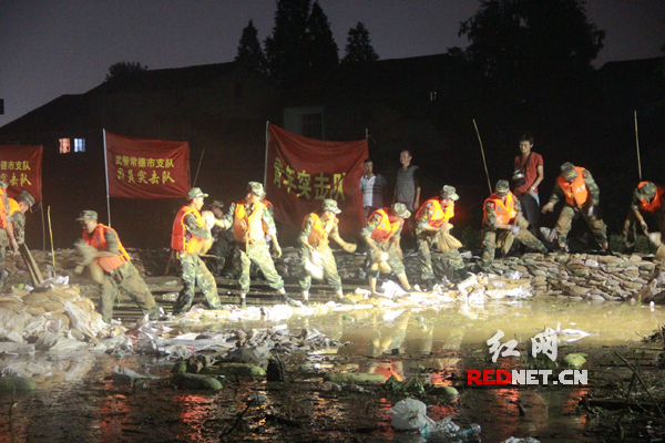 官兵冒着雷电和大雨传递沙袋搭建围堰。