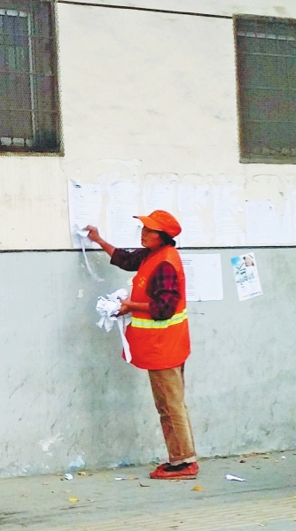 一名环卫工正在撕张贴在临街墙上的通告