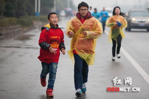 有许多小朋友选择了参加1/4长的马拉松比赛，图为一名小朋友与一名参赛选手一起跑步。
