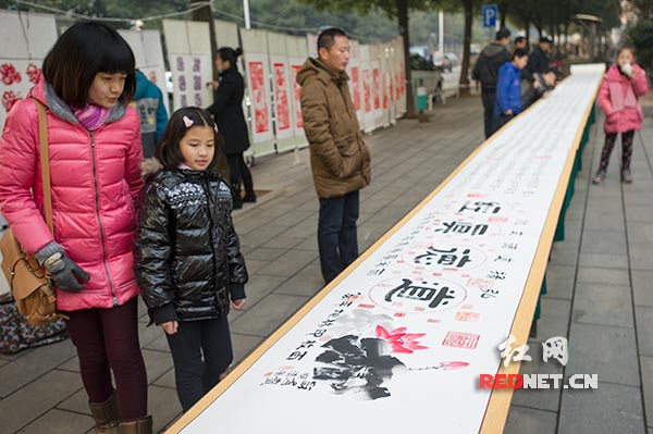 社区居民纷纷停下脚步，细细观看展示在街边的书法家朱长生创作的《道德经》百米隶书长卷。