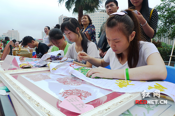 浏阳市残联组织的姑娘们在现场绣十字绣。桌上是浏阳市特殊教育学校学生制作的剪纸。