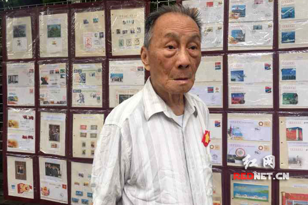 刘建本站在自己收集的邮票墙前追忆历史