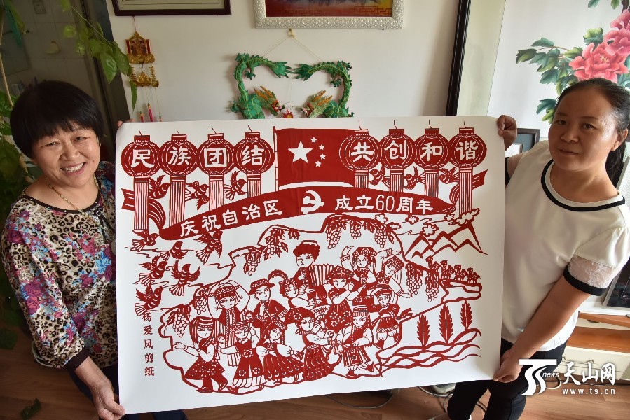 爱凤(左一)展示刚刚完成的一副主题为"民族团结 共创和谐"的剪纸作品