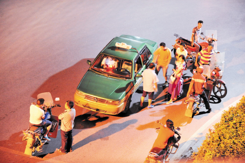 一些无牌的士和摩的围住一名女乘客，一名负责维持秩序的保安却在和非法营运者聊天。