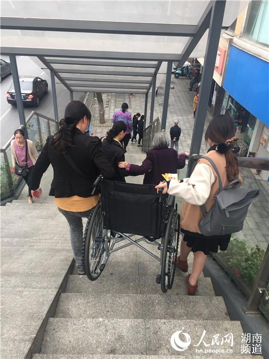 因无法使用垂直电梯，病患家属只能求助路人帮抬轮椅