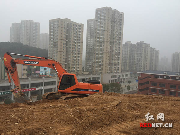 整改的自然山体旁边是高楼和在建学校。