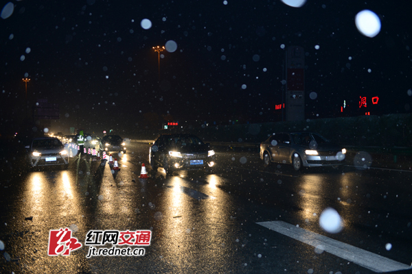 2月1日晚，邵怀高速洞口服务区出口飘落大雪，高速路政员指挥车辆有序通行。
