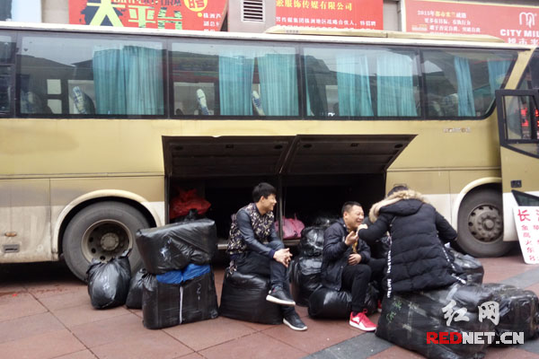 在市场群待客的大客车行李箱前堆满了打好包的服装包裹。