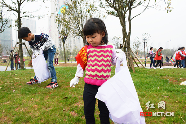 佩戴志愿袖章的小朋友提着垃圾袋捡垃圾。