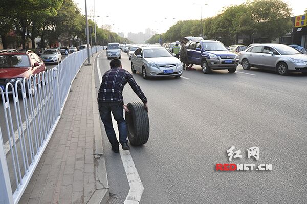 25日下午5:30左右，长沙市民车女士车辆在行驶过程中车轮突然飞出，车辆瘫痪在马路中间。图为前来救援的师傅将远处车轮捡回安装。