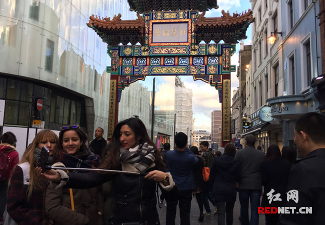三名英国女孩在伦敦唐人街“英伦吉祥”的牌楼前自拍，目前有50万华人华侨和留学生生活在英国。