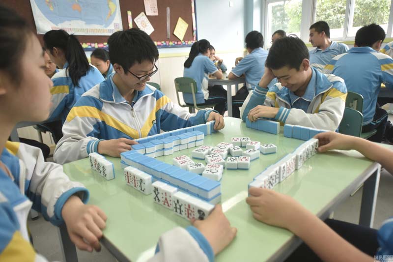 2016年5月31日,四川省成都市机投中学,中考即将来临,机投中学的初三学生竟然在教室里玩起了“麻将”。原来学生们玩的“麻将”并非传统麻将,而是校长田精耘发明的“英语麻将”。这种麻将是一种独特的英语教具,以麻将为载体,在麻将的正面贴上了英文字母,学生通过对不同的麻将进行组合,最后可以拼成不同的单词。这样不仅可以帮助学生记忆单词,同时也锻炼了学生的词根联想记忆能力。不仅是麻将,扑克牌和围棋上也都是英文字母,并且学生们每出一次牌、走一步棋,都会在自己的本子上记下一个单词,最后,谁的单词多谁就是“赢家”。图为初三学生们在教室里玩“英语麻将”减压。