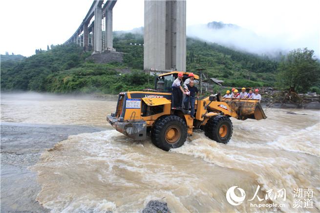 由于道路被洪水冲垮，工作人员只能通过铲车过河 石可君摄