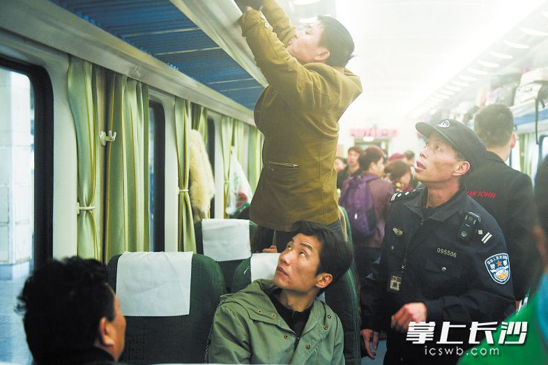 昨日，在从长沙开往海口的火车上，乘警朱立山提醒旅客把行李箱放置好。 长沙晚报记者 黄启晴 摄