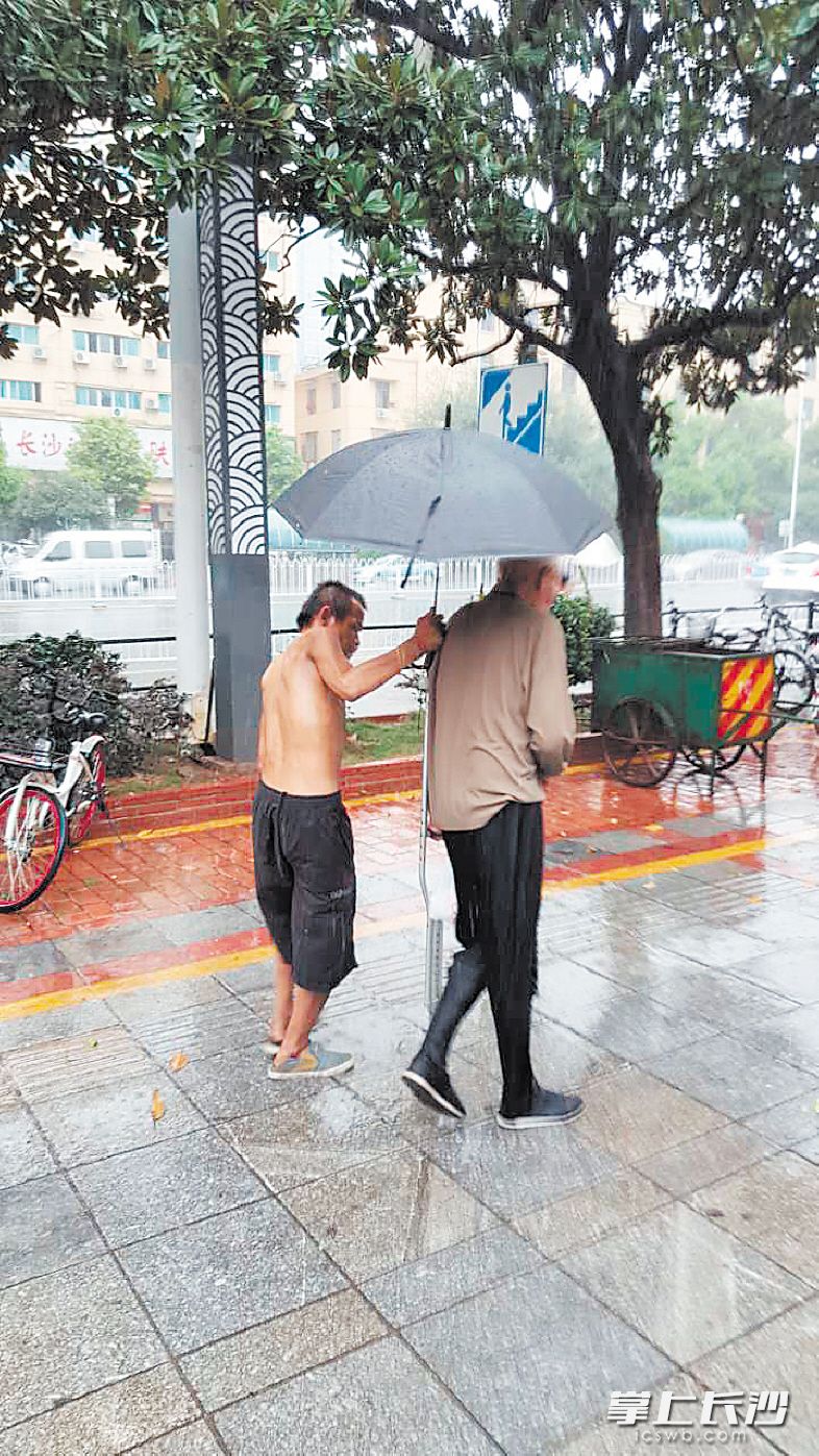 前日，这位上身赤膊的残疾人虽然自己一瘸一拐，但仍为拄拐老人撑伞。目击者杨树雄 摄